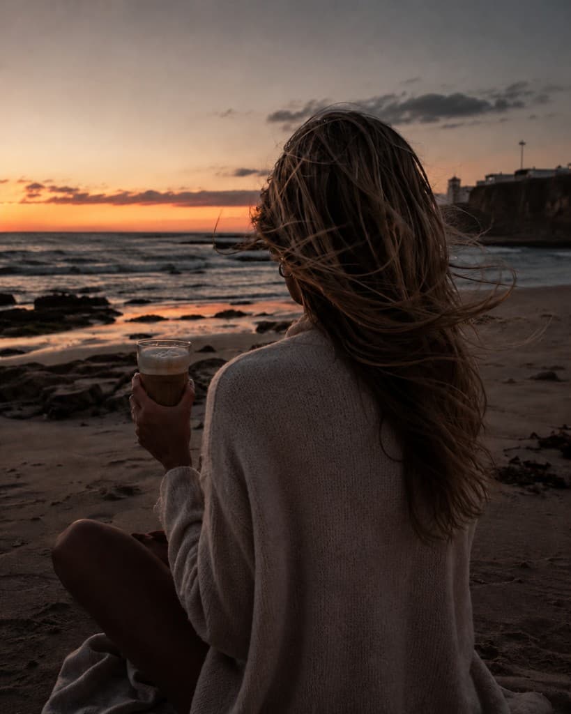 Frau am Strand bei Sonnenuntergang mit Kaffee
